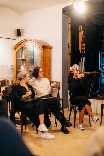 Tři ženy sedí na židlích. Jedna z žen komunikuje ve znakovém jazyce.