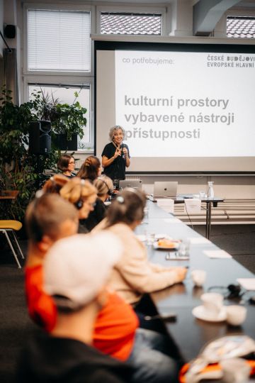 Prezentace o přístupnosti kulturních prostor, přednášející žena mluví k účastníkům workshopu.