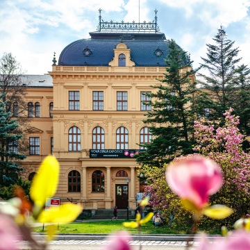 The facade of the historical South Bohemian Museum building, with trees and flowers in the foreground.
