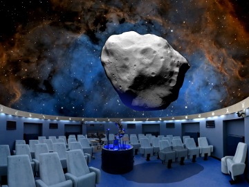 The planetarium hall with a space projection and an asteroid model that appears to float above the blue seats.